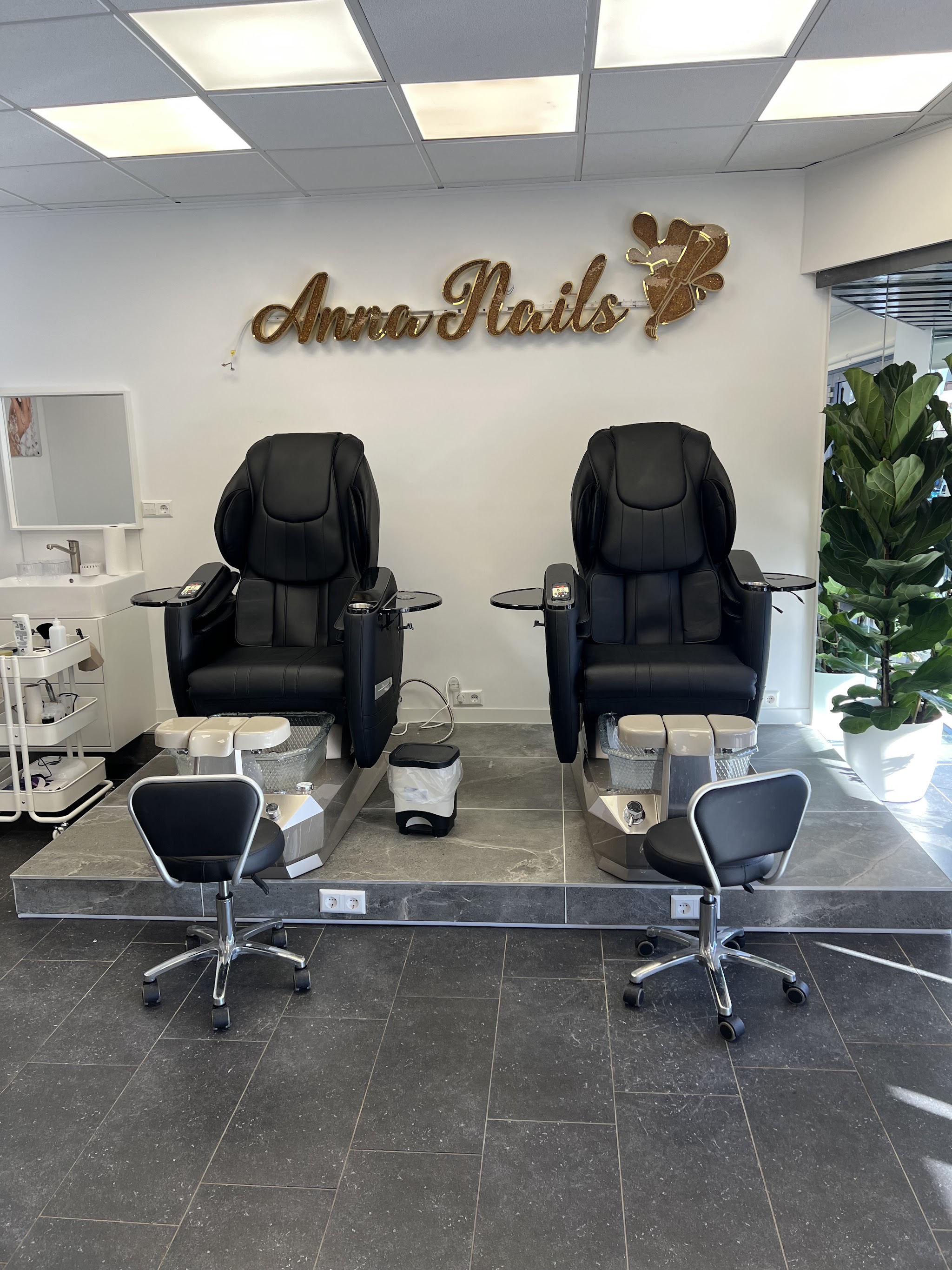 De salon met twee zwarte massagestoelen voor de pedicure onder de gouden letters Anna Nails